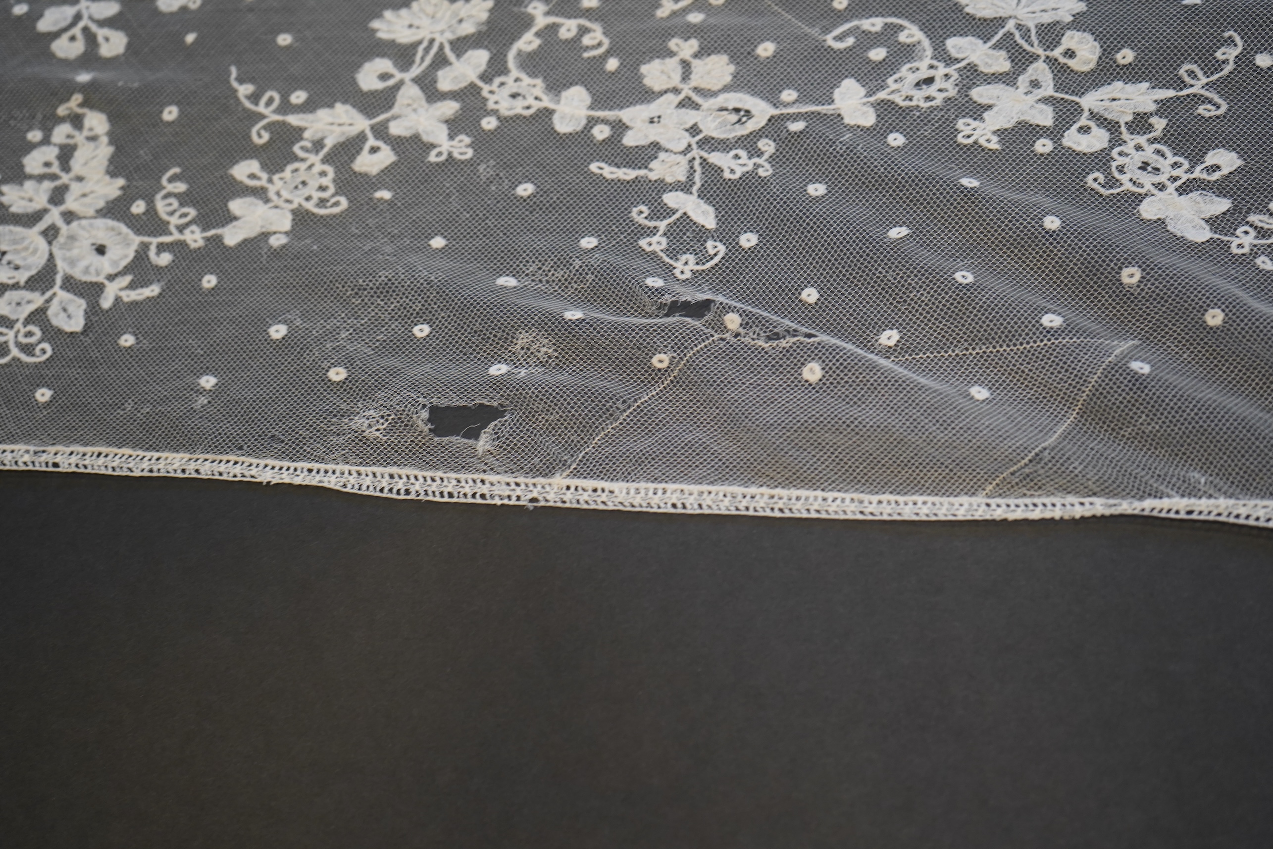 A deep elaborately designed flounce of mid 19th century Brussels bobbin appliquéd lace on net, with finished lace ends, worked with an intricate floral border below large floral cartouches framed in similar motifs and al